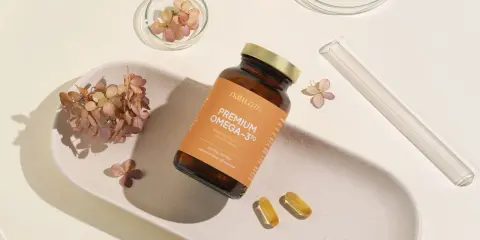 Butelka z suplementem omega 3 dla niemowląt, dwie kapsułki i suszone kwiaty na ceramicznej tacce.