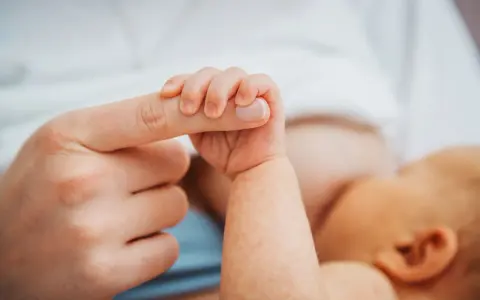 Dłoń noworodka ściska palec dorosłego. Delikatny uścisk, który budzi pytanie: czy można przekarmić noworodka?