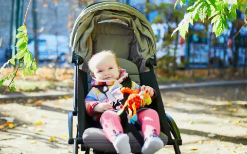 Uśmiechnięte dziecko w wózku, trzymające kolorową zabawkę. Czas na spacer, do kiedy gondola posłuży maluchowi?