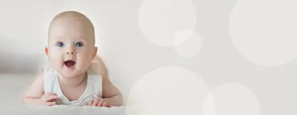Uśmiechnięte niemowlę 4 miesiące leży na brzuchu, z otwartymi ustami i szeroko otwartymi oczami, patrząc wprost na widza.